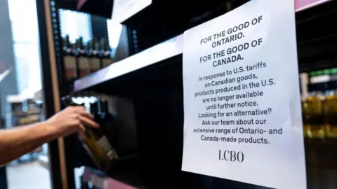 Getty Images A worker is seen removing US liquor off shelves in Ontario, next to a sign that reads "FOR THE GOOD OF ONTARIO. FOR THE GOOD OF CANADA. In response to US tariffs on Canadian goods, products produced in the US are no longer available until further notice."