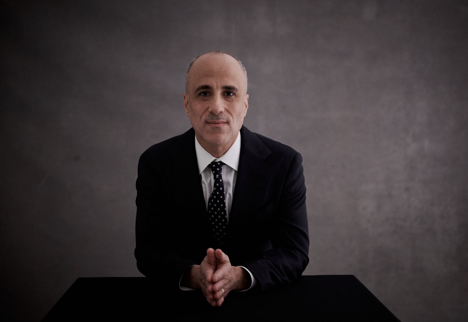 Drew Warshaw, candidate for NY State Comptroller, sitting at a table with hands clasped.