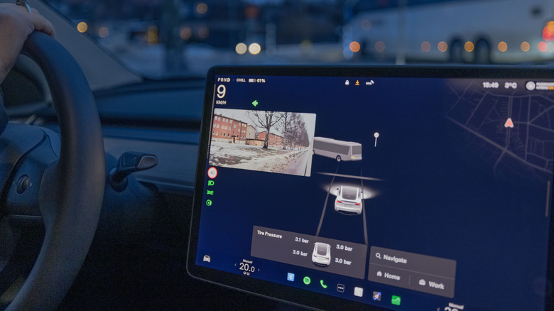 Sweden. Uppsala. January 15, 2025. Female driver in Tesla Model Y electric car using autopilot with side camera view on winter street.