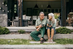 An older man and woman sitting on outdoor steps holding mugs and smiling