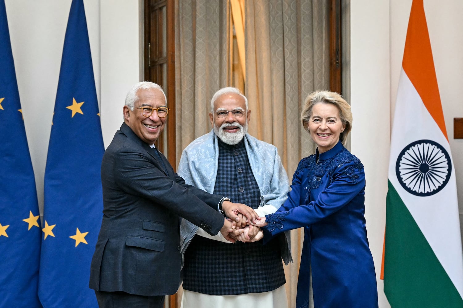 European Council President António Costa, Indian Prime Minister Narendra Modi, and European Commission President Ursula von der Leyen hold hands in front of flags of the European Union and India.