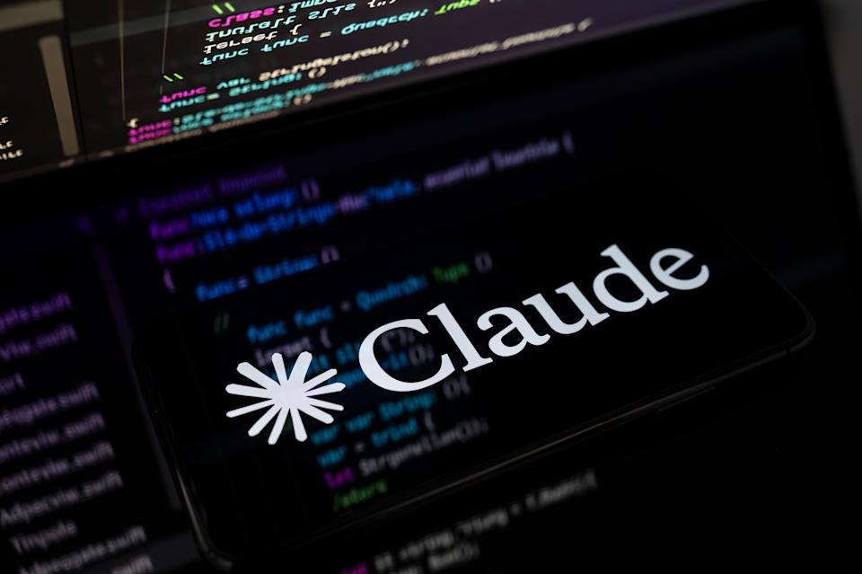 The Claude AI logo is displayed on the screen of a smartphone placed on a reflective surface onto which lines of computer code are projected. Following the release of Claude Opus 4.6 on February 5, Anthropic continues to challenge its main competitors in the generative AI market in Creteil, France, on February 6, 2026. (Photo by Samuel Boivin/NurPhoto via Getty Images)