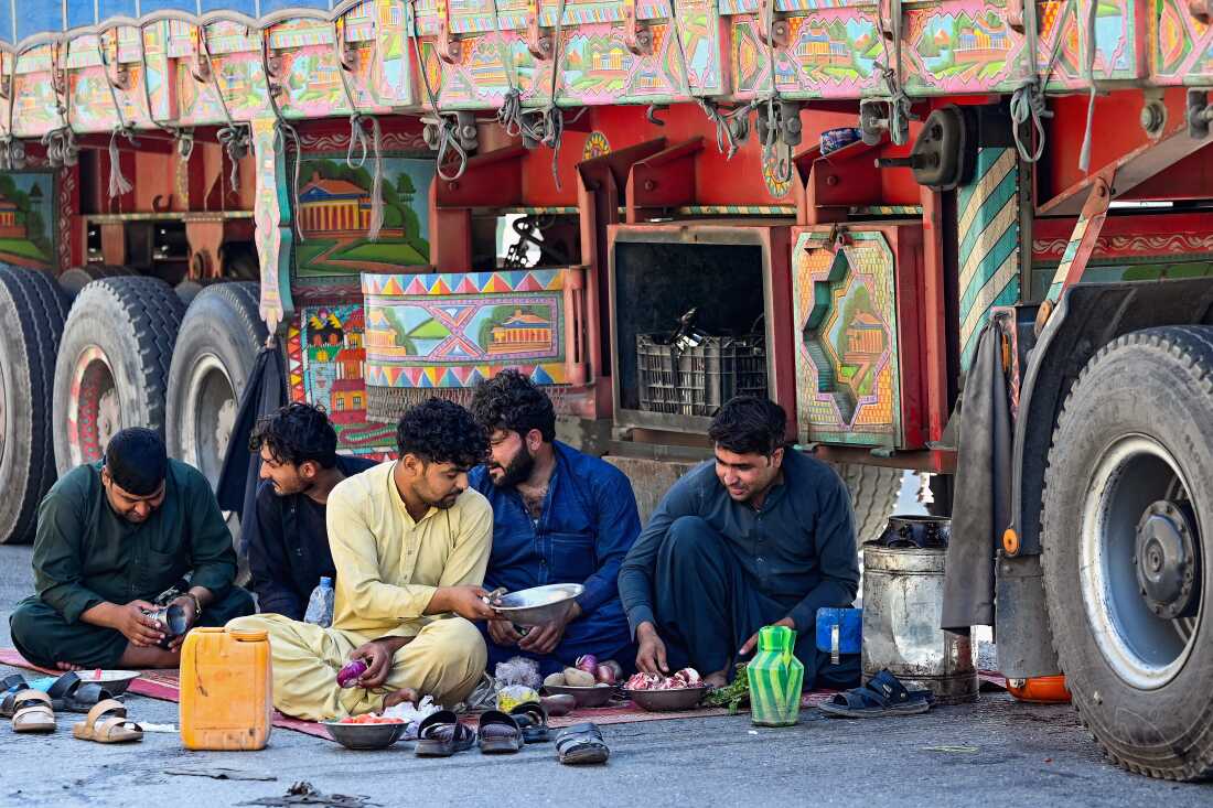 Truck drivers eat on the ground by their stalled vehicles near Torkham, Pakistan, on Oct. 13, 2025. More than three months later, the Torkham border remains closed with no end in sight.